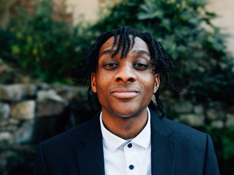 Young man smiling confidently in a blue suit outdoors with greenery background, Atlanta.
