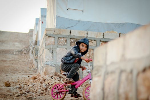 Young child rides a bicycle in a refugee camp in Idlib, Syria, portraying resilience and playfulness.