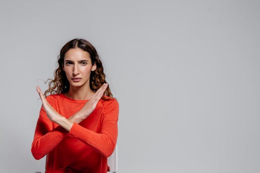 Woman with crossed arms making an X gesture against a gray background, indoor portrait.